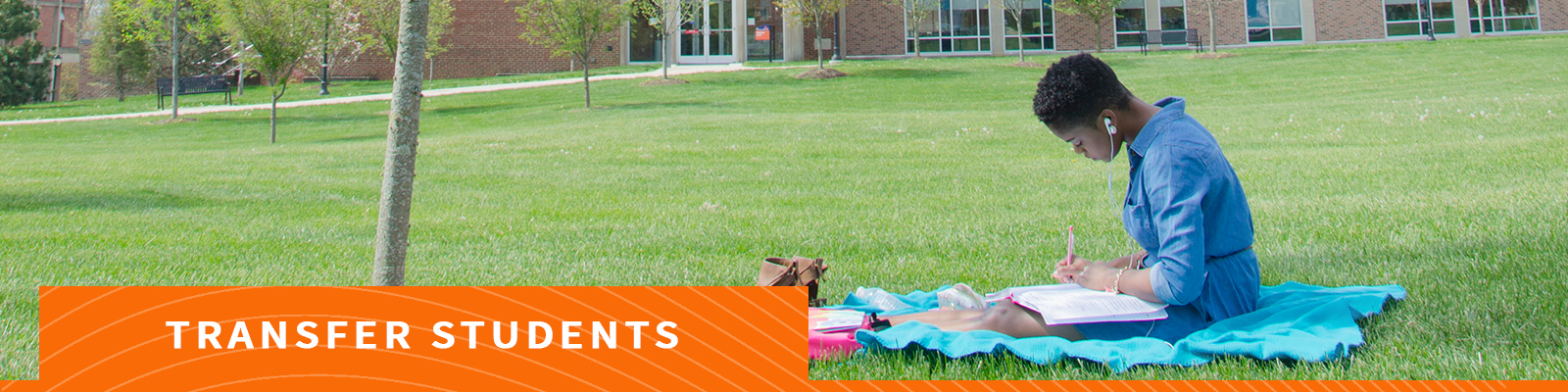 Student studying on blanket in grass area on campus