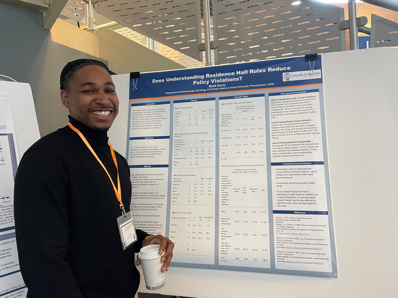 A male student smiling beside his poster