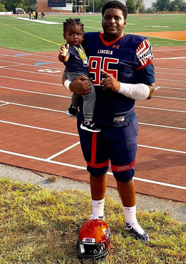 Jamain Pink in football gear holding his toddler son