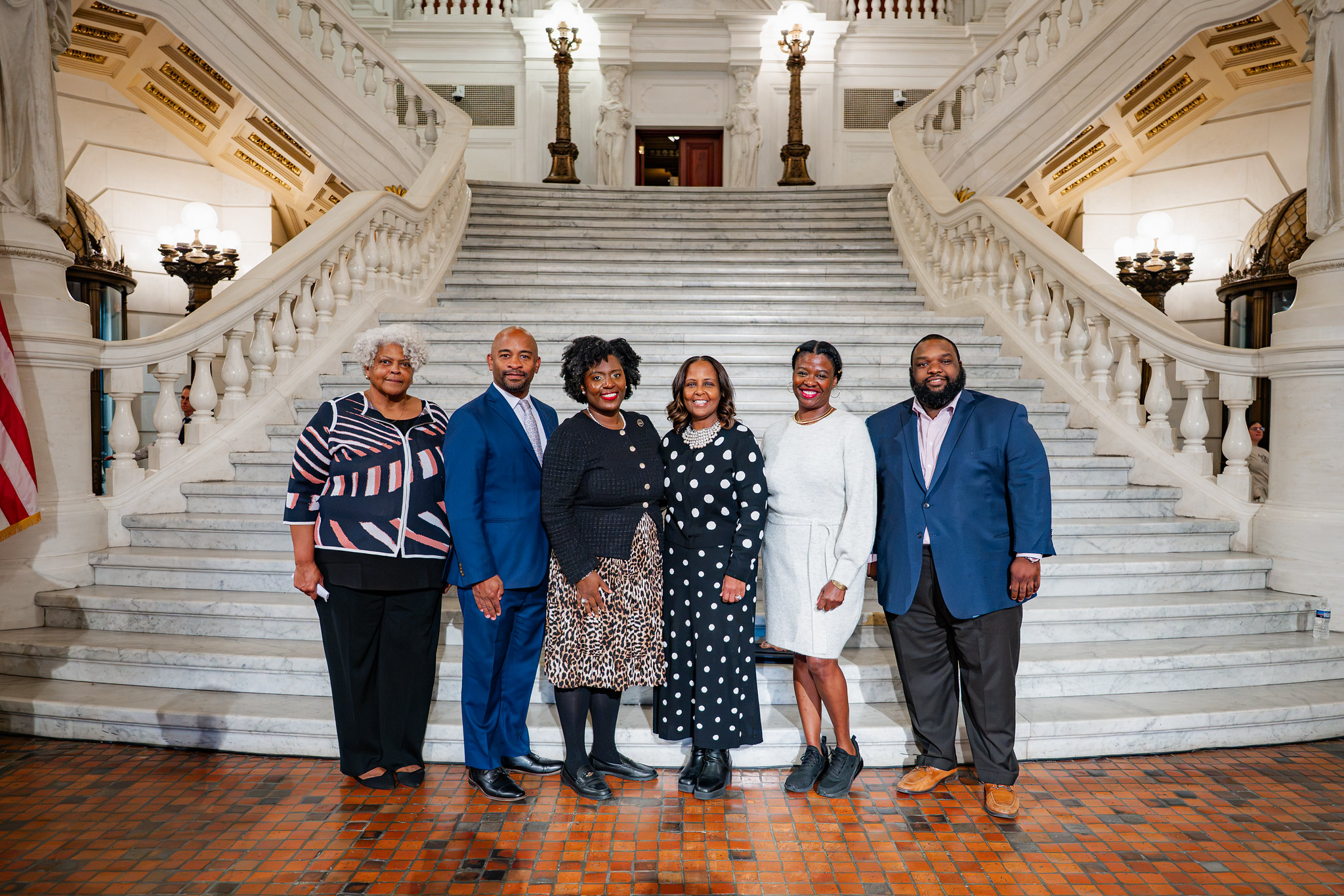 Group of six people standing in front of grand staircase smiling at camera 1